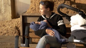 Bebê de alimentação positivo e sorrindo da mamãe exterior em um banco que tem o resto imagens de stock Bebê de alimentação positivo e sorrindo da mamãe exterior em um banco que tem o resto imagens de stock
