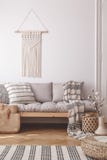 Beige handgjord makramé på en vit vägg ovanför en soffa med en randig linnekudde i en naturlig vardagsruminre arkivfoton Beige handgjord makramé på en vit vägg ovanför en soffa med en randig linnekudde i en naturlig vardagsruminre arkivfoton