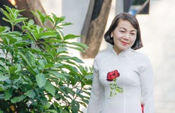 Bella donna asiatica di mezza età che sorride in un vestito bianco con una rosa rossa ricamata fotografia stock Bella donna asiatica di mezza età che sorride in un vestito bianco con una rosa rossa ricamata fotografia stock
