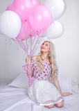 Bella donna bionda con i palloni rosa e bianchi Emozioni allegre celebrazione Una bella bionda sta sedendosi su un letto con il r fotografia stock Bella donna bionda con i palloni rosa e bianchi Emozioni allegre celebrazione Una bella bionda sta sedendosi su un letto con il r fotografia stock