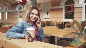Bella giovane donna felice che si siede in caffè e che parla sul telefono video d archivio Bella giovane donna felice che si siede in caffè e che parla sul telefono video d archivio
