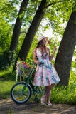 Bella giovane donna in un vestito ed in un cappello su una bicicletta sul nazionale Fotografia Stock Bella giovane donna in un vestito ed in un cappello su una bicicletta sul nazionale Fotografia Stock