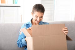 Belle boîte d'ouverture de jeune femme avec le colis tout en se reposant sur le sofa à la maison image libre de droits Belle boîte d'ouverture de jeune femme avec le colis tout en se reposant sur le sofa à la maison image libre de droits