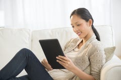 Belle femme à l'aide de la Tablette de Digital tout en détendant sur le sofa photographie stock libre de droits Belle femme à l'aide de la Tablette de Digital tout en détendant sur le sofa photographie stock libre de droits