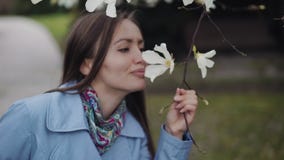 Belle fille avec un sourire examine les fleurs blanches de magnolia et les reniffe clips vidéos Belle fille avec un sourire examine les fleurs blanches de magnolia et les reniffe clips vidéos