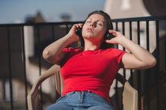 Belle fille dans un T-shirt rouge et des écouteurs Une fille sur le balcon écoutant la musique et chante Images stock Belle fille dans un T-shirt rouge et des écouteurs Une fille sur le balcon écoutant la musique et chante Images stock