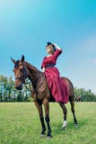 Belle fille dans une longue robe rouge montant un cheval brun contre un ciel bleu photos stock Belle fille dans une longue robe rouge montant un cheval brun contre un ciel bleu photos stock