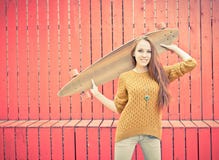 Belle fille de roux tenant un longboard se tenant près du mur rouge photo libre de droits Belle fille de roux tenant un longboard se tenant près du mur rouge photo libre de droits