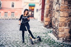 Bello messaggio di testo di scrittura della donna mentre guidando motorino elettrico sulle vie urbane immagini stock libere da diritti Bello messaggio di testo di scrittura della donna mentre guidando motorino elettrico sulle vie urbane immagini stock libere da diritti