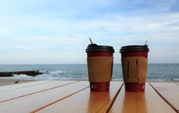 Beschikbare koppen die van koffie zich op een lijst tegen het blauwe overzees bevinden Koffiekop op Houten lijstbovenkant op het stock fotografie Beschikbare koppen die van koffie zich op een lijst tegen het blauwe overzees bevinden Koffiekop op Houten lijstbovenkant op het stock fotografie