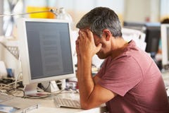 Betonter Mann, der am Schreibtisch im beschäftigten kreativen Büro arbeitet Betonter Mann, der am Schreibtisch im beschäftigten kreativen Büro arbeitet
