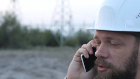 Bevindt de post technische directeur zich in een witte helm dichtbij de krachtcentrale en het spreken op de telefoon met de arbei stock video Bevindt de post technische directeur zich in een witte helm dichtbij de krachtcentrale en het spreken op de telefoon met de arbei stock video