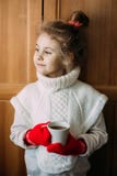 Bezauberndes siebenjähriges Mädchen trinkt den warmen Tee und steht nahe bei dem Fenster Sie trägt eine warme gestrickte Strickja stockfotografie Bezauberndes siebenjähriges Mädchen trinkt den warmen Tee und steht nahe bei dem Fenster Sie trägt eine warme gestrickte Strickja stockfotografie