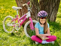 Bicycle girl wearing helmet read book on rest near . Stock Photo Bicycle girl wearing helmet read book on rest near . Stock Photo