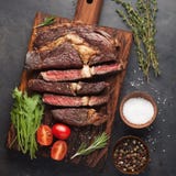 Bife grelhado do ribeye com vinho tinto, ervas e especiarias em um fundo de pedra escuro Vista superior com espaço da cópia para imagens de stock Bife grelhado do ribeye com vinho tinto, ervas e especiarias em um fundo de pedra escuro Vista superior com espaço da cópia para imagens de stock