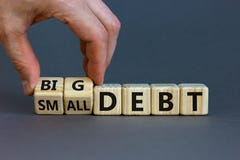 Big or small debt symbol. Businessman turns a wooden cube and changes words `small debt` to `big debt`. Beautiful grey table,