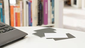 Biglietti da visita in bianco e un computer portatile davanti ad uno scaffale per libri vago fotografia stock Biglietti da visita in bianco e un computer portatile davanti ad uno scaffale per libri vago fotografia stock