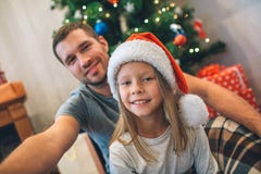 Bild av fadern och dottern som sitter på golv De ser raka och leendet Den unga mannen rymmer kameran De tar selfie royaltyfri bild Bild av fadern och dottern som sitter på golv De ser raka och leendet Den unga mannen rymmer kameran De tar selfie royaltyfri bild