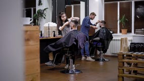 Bild av inre av frisersalongen och två yrkesmässiga frisörer Kvinnliga och manliga barberare som arbetar med att sitta för klient arkivfilmer Bild av inre av frisersalongen och två yrkesmässiga frisörer Kvinnliga och manliga barberare som arbetar med att sitta för klient arkivfilmer