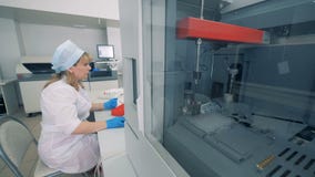 Biochemical analyzer is testing samples and a female worker is controlling the process. 4K Biochemical analyzer is testing samples and a female worker is controlling the process. 4K