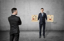 Biznesmen patrzeje innego mężczyzna trzyma dwa pudełka z patroszonymi twarzami z obracam z powrotem na betonowym tle obraz stock Biznesmen patrzeje innego mężczyzna trzyma dwa pudełka z patroszonymi twarzami z obracam z powrotem na betonowym tle obraz stock
