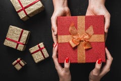 On a black background, a man`s hands carry a red gift in the hands of a young lady. Holiday card. Stock Photos On a black background, a man`s hands carry a red gift in the hands of a young lady. Holiday card. Stock Photos