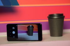Black paper Cup with plastic lid. coffee or takeaway on a violet and pink background. brutal glass with mobile phone stock image Black paper Cup with plastic lid. coffee or takeaway on a violet and pink background. brutal glass with mobile phone stock image