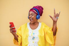 Black senior woman on traditional african dress dancing to rock music on mobile phone - Focus on face