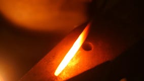 A Blacksmith Picks Up a Massive Hammer and Start Banging Hot Metal Bar on Anvil in Slow Motion