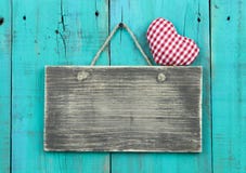 Blank distressed wood sign with red checkered heart hanging on rustic antique teal blue door