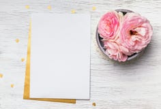 Blank paper and cute pink flowers on white wooden table