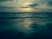 Blauer Sonnenuntergang unter einem bewölkten Himmel auf einem sandigen Strand mit Reflexionen auf dem nass Sand lizenzfreies stockbild Blauer Sonnenuntergang unter einem bewölkten Himmel auf einem sandigen Strand mit Reflexionen auf dem nass Sand lizenzfreies stockbild