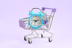 Blauwe wekker in supermarktkarretje op violette achtergrond royalty-vrije stock afbeeldingen Blauwe wekker in supermarktkarretje op violette achtergrond royalty-vrije stock afbeeldingen