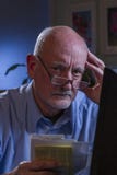 Blicke des älteren Mannes gesorgt, wie er die Lohnlisten, die on-line sind, vertikal Lizenzfreies Stockfoto