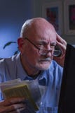 Blicke des älteren Mannes gesorgt, wie er die Lohnlisten, die on-line sind, vertikal Stockbild