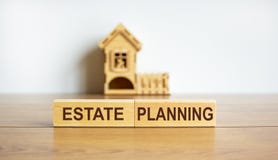 Blocks form the words `estate planning` in front of a miniature house. Copy space. Business concept