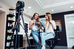 Bloggers fêmeas de sorriso da beleza que reveem produtos de composição para seu blogue que grava um vídeo na câmera no salão de b fotografia de stock Bloggers fêmeas de sorriso da beleza que reveem produtos de composição para seu blogue que grava um vídeo na câmera no salão de b fotografia de stock
