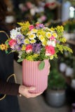 Blomsterhandlare som rymmer en vas med härlig blommaordning av rosa rosor, lila aster, vita krysantemum och andra växter i royaltyfri bild Blomsterhandlare som rymmer en vas med härlig blommaordning av rosa rosor, lila aster, vita krysantemum och andra växter i royaltyfri bild