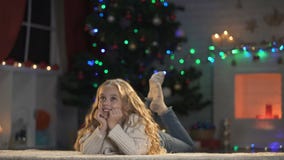 Blond flicka som ligger på golvet som tänker om X-mas beröm, väntande på gåvor Blond flicka som ligger på golvet som tänker om X-mas beröm, väntande på gåvor