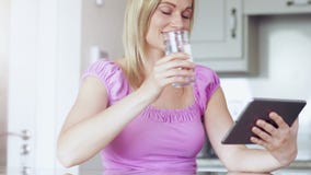 Blonde drinking glass of water using tablet