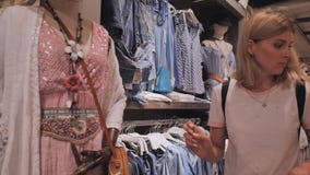 Blonde girl chooses things in the women`s clothing store. stock footage Blonde girl chooses things in the women`s clothing store. stock footage