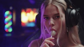 Blonde sexy gamer girl streamer puts a lollipop in her mouth while looking in the camera