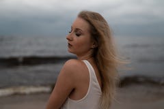 Close up portrait of Beautiful young blonde woman beach nymph in white dress near sea with waves during a dull gloomy royalty free stock photo Close up portrait of Beautiful young blonde woman beach nymph in white dress near sea with waves during a dull gloomy royalty free stock photo