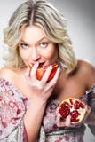 Blonde Woman Biting Pomegranate On Gray Royalty Free Stock Photography
