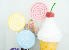 Blondes Mädchen, das auf verziertem Hintergrund mit großen Spielzeuglutschern und Eiscreme aufwirft lizenzfreies stockbild Blondes Mädchen, das auf verziertem Hintergrund mit großen Spielzeuglutschern und Eiscreme aufwirft lizenzfreies stockbild