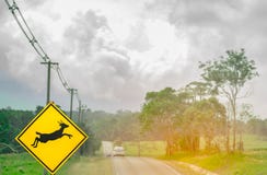 Blue SUV car of the tourist driving with caution during travel at asphalt road near yellow traffic sign with deer jumping inside. The sign Royalty Free Stock Photos Blue SUV car of the tourist driving with caution during travel at asphalt road near yellow traffic sign with deer jumping inside. The sign Royalty Free Stock Photos