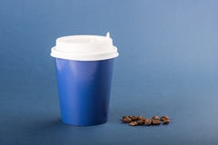 Blå disponibel kopp med vita lock- och kaffebönor på en blå bakgrund royaltyfri bild Blå disponibel kopp med vita lock- och kaffebönor på en blå bakgrund royaltyfri bild