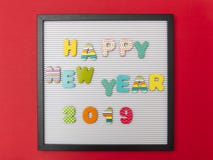 Board with black frame, text happy new year 2019 in colorful letters, red wall background stock photos Board with black frame, text happy new year 2019 in colorful letters, red wall background stock photos