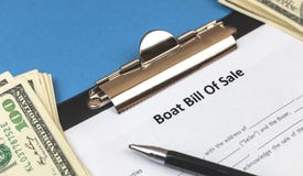 Boat bill of sale agreement contract form on clipboard close-up. Office table with pen and money. Concept of buying or
