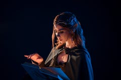 Boczny widok tajemniczy żeński piękny elf czyta magiczną książkę w ciemności obrazy stock Boczny widok tajemniczy żeński piękny elf czyta magiczną książkę w ciemności obrazy stock